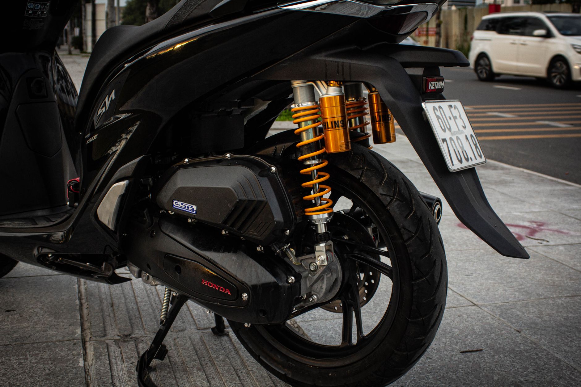 Detailed view of a motorcycle's rear wheel and suspension system on a city street.