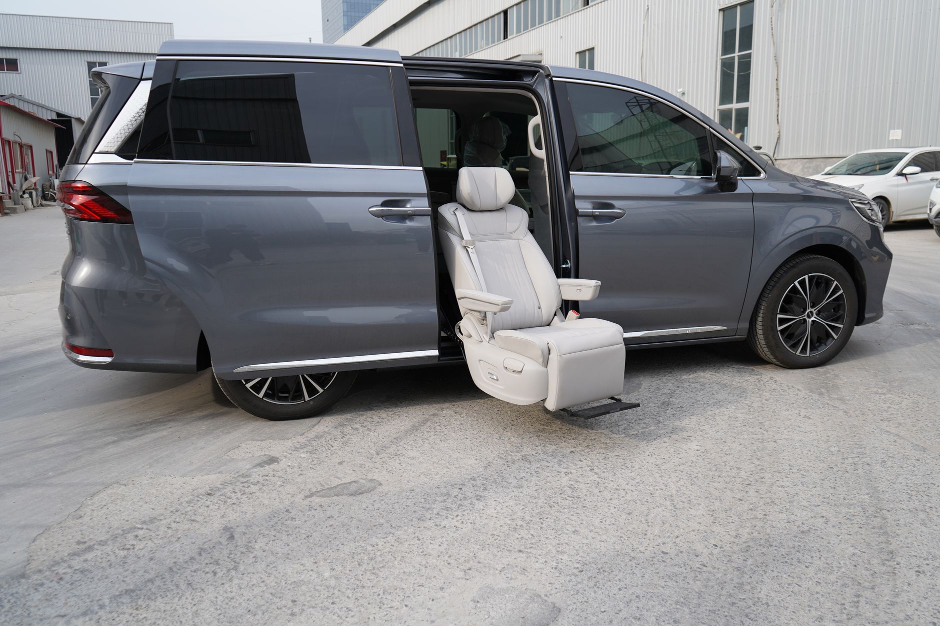 Gray luxury minivan featuring an open door with a reclining massage seat in an urban setting, showcasing comfort and style.