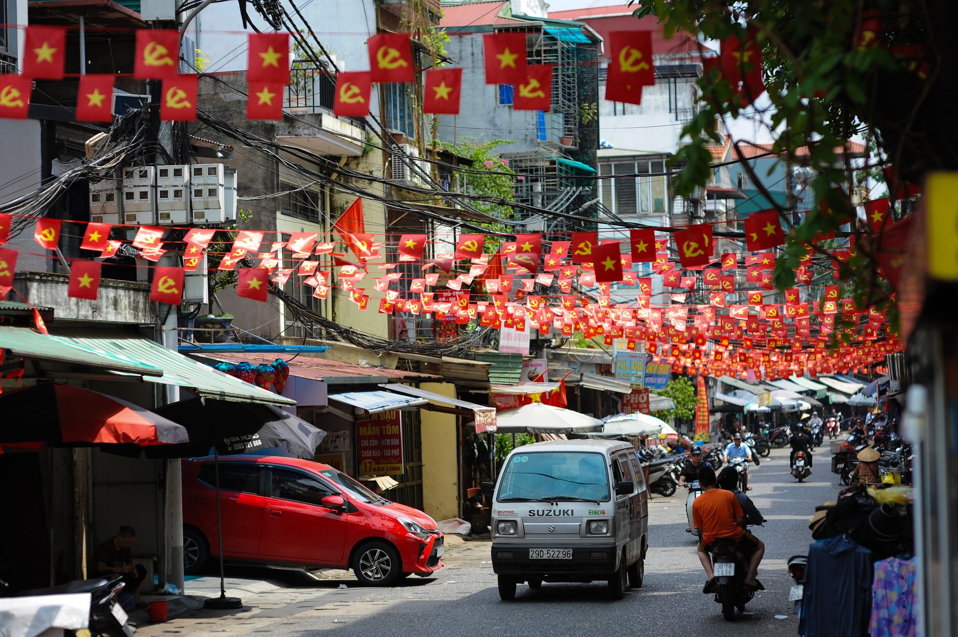 Vibrant Vietnamese street adorned with communist and national flags, bustling with locals and vehicles.