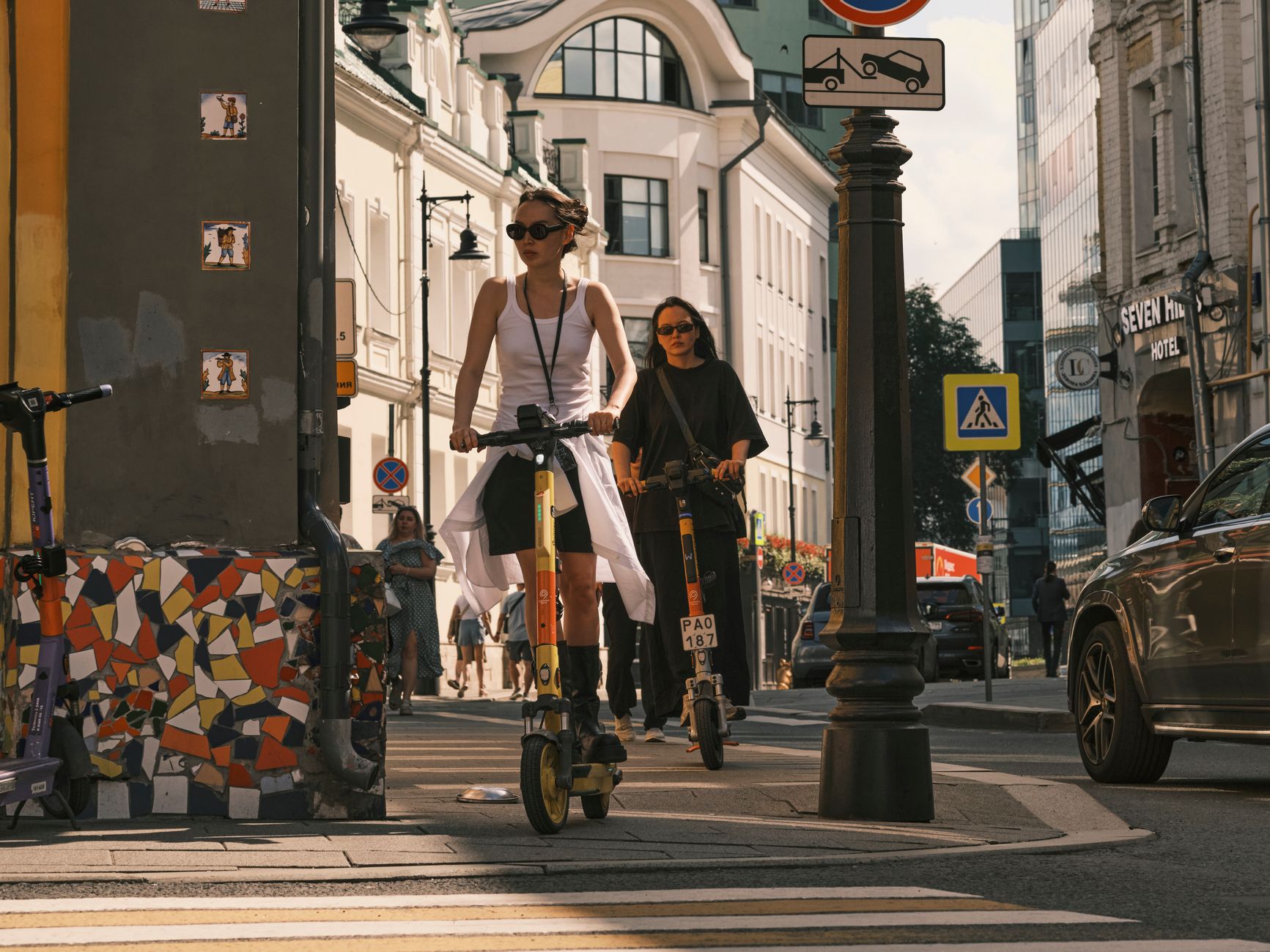Two women riding electric scooters on a city street, showcasing urban commute.