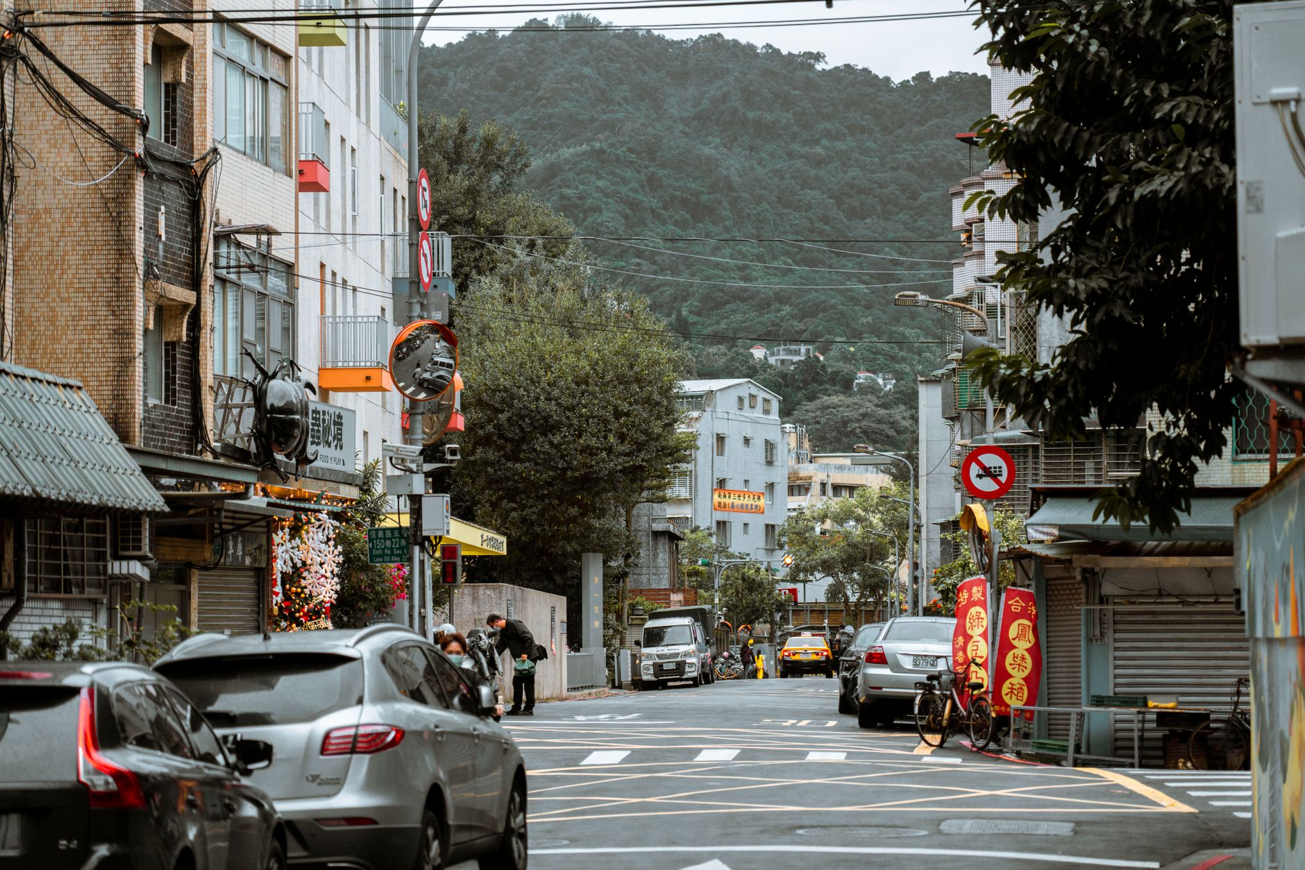 Vibrant city street bustling with cars and pedestrians, nestled against a lush mountain backdrop.