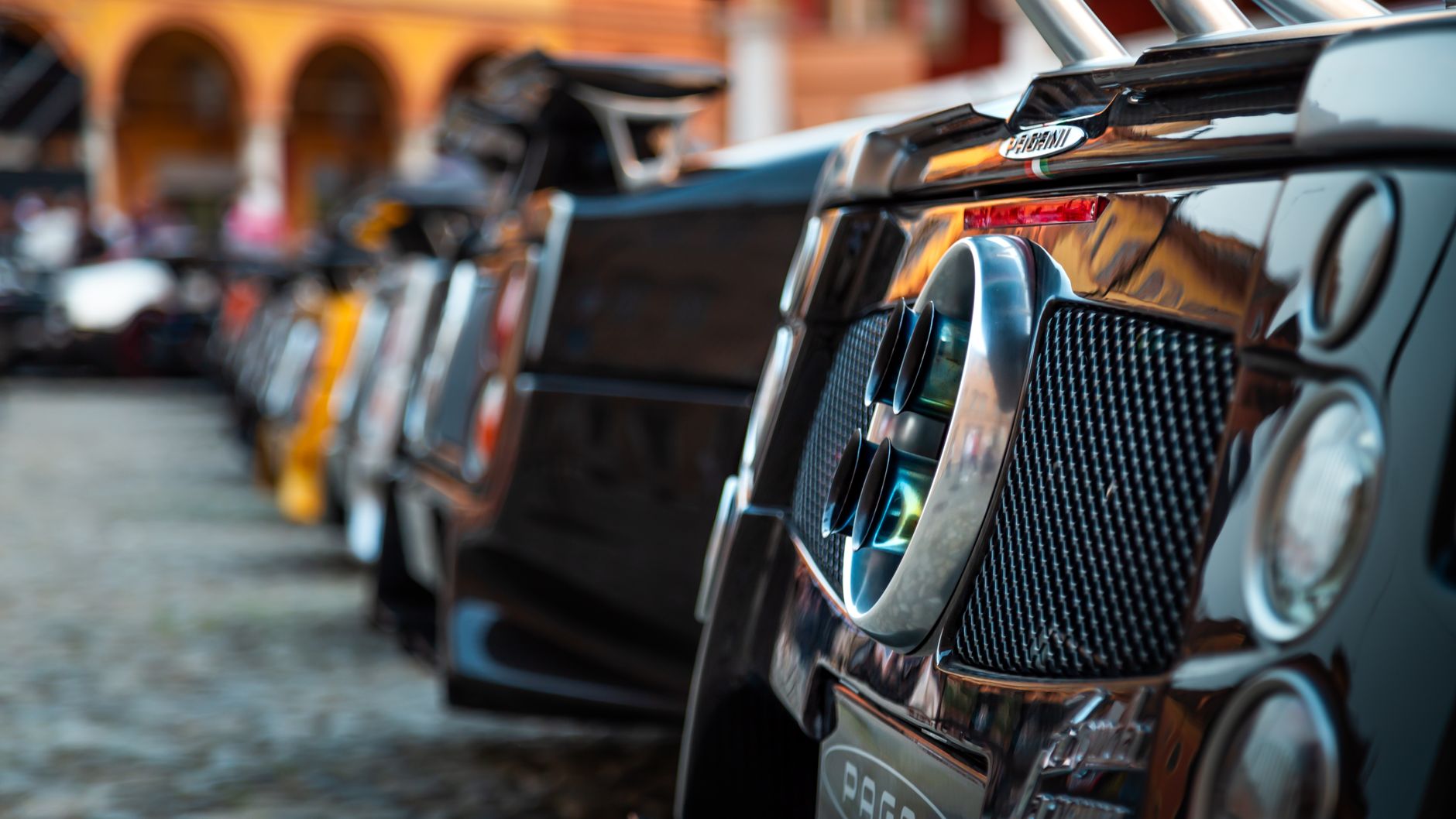 Detailed close-up of a Pagani supercar's rear end with other hypercars lined up outdoors.
