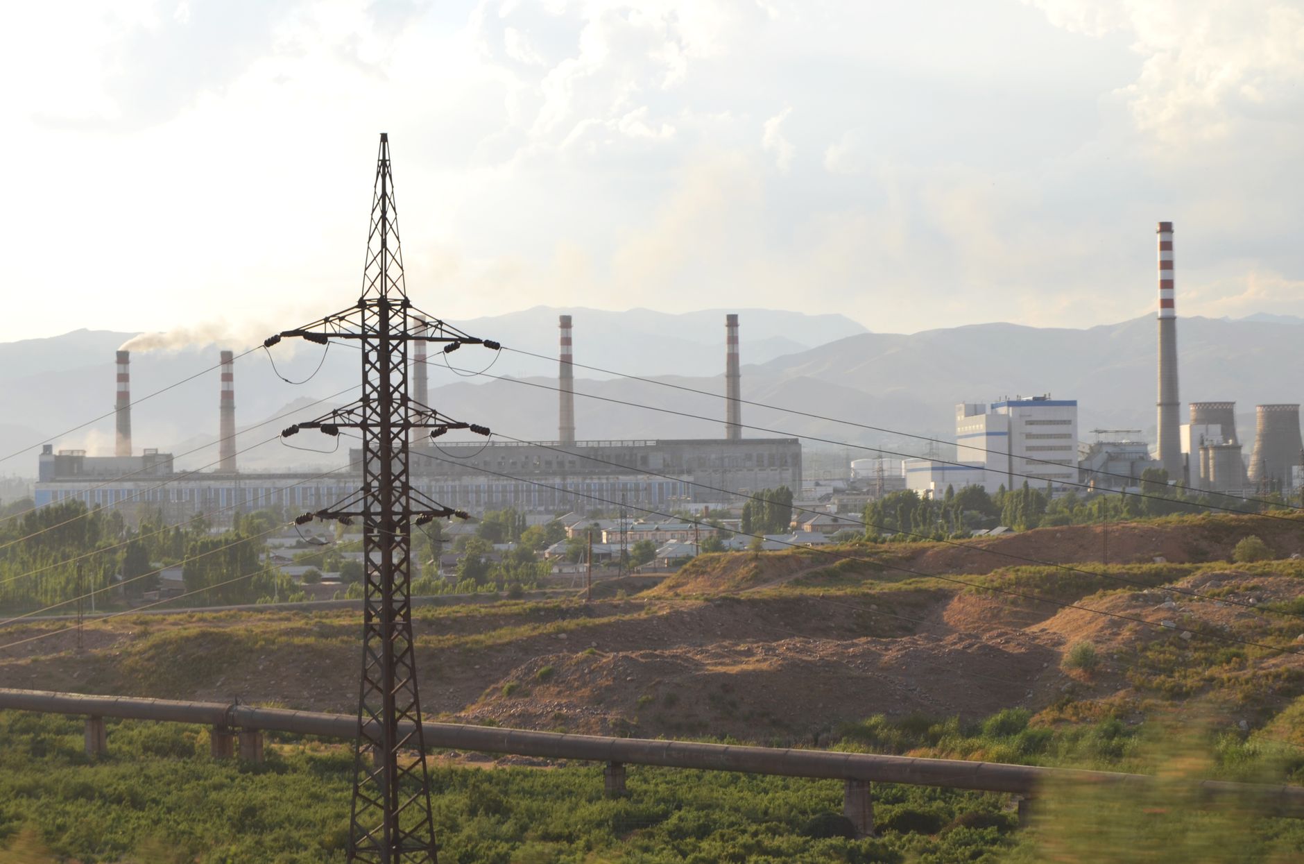 A view of an industrial power plant with an electricity pylon and smokestacks in the background.
