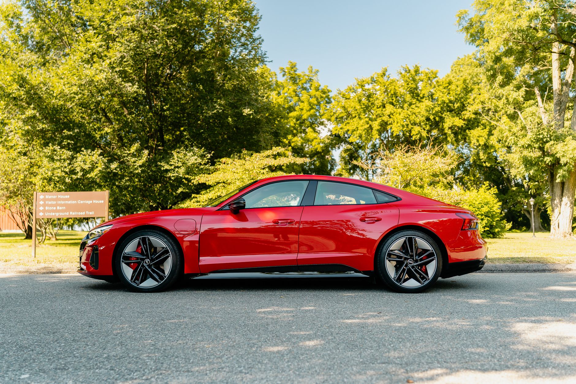Side view of a luxury red sedan parked outdoors on a sunny day surrounded by greenery.