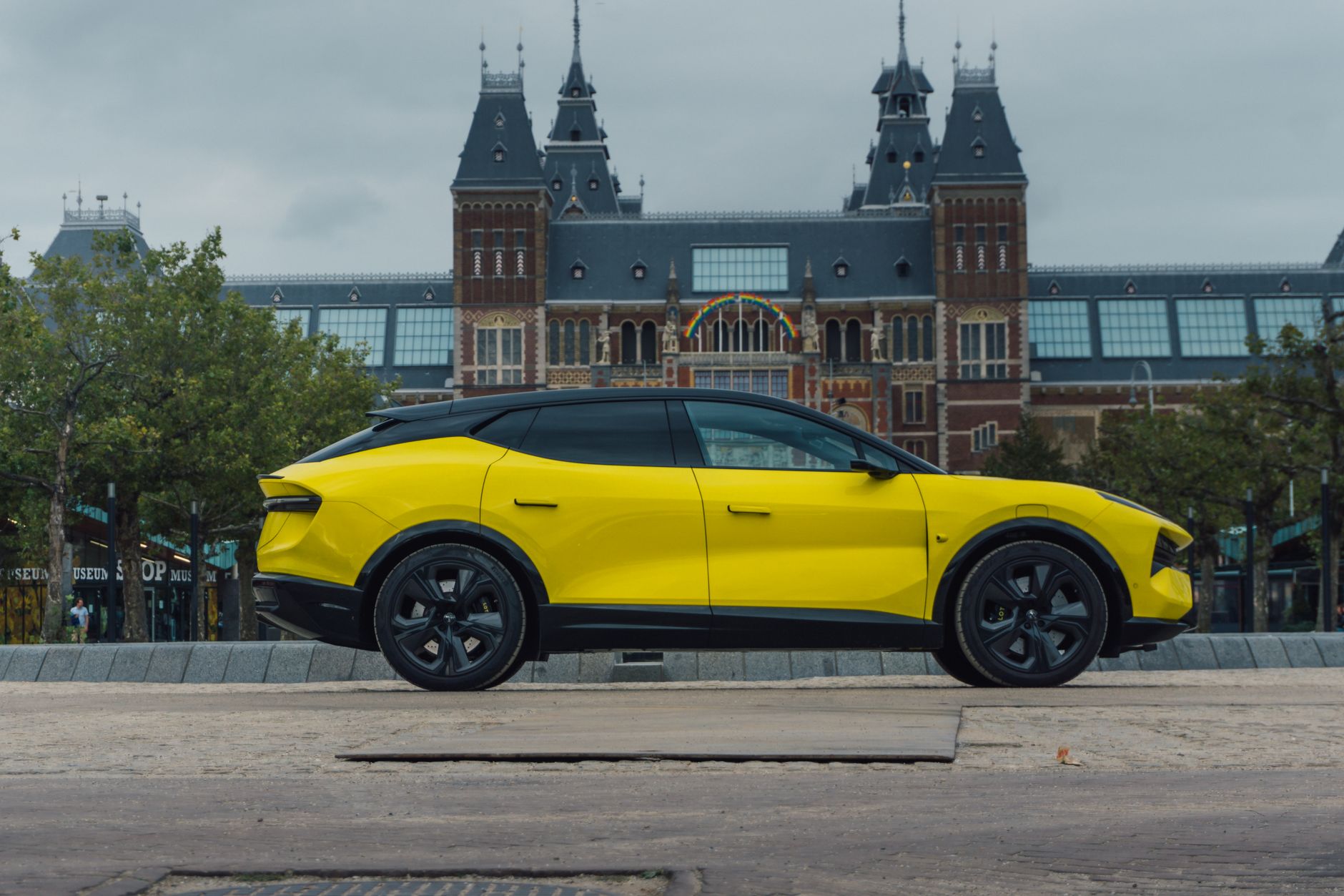 A modern yellow electric car parked in front of the historic Rijksmuseum in Amsterdam.