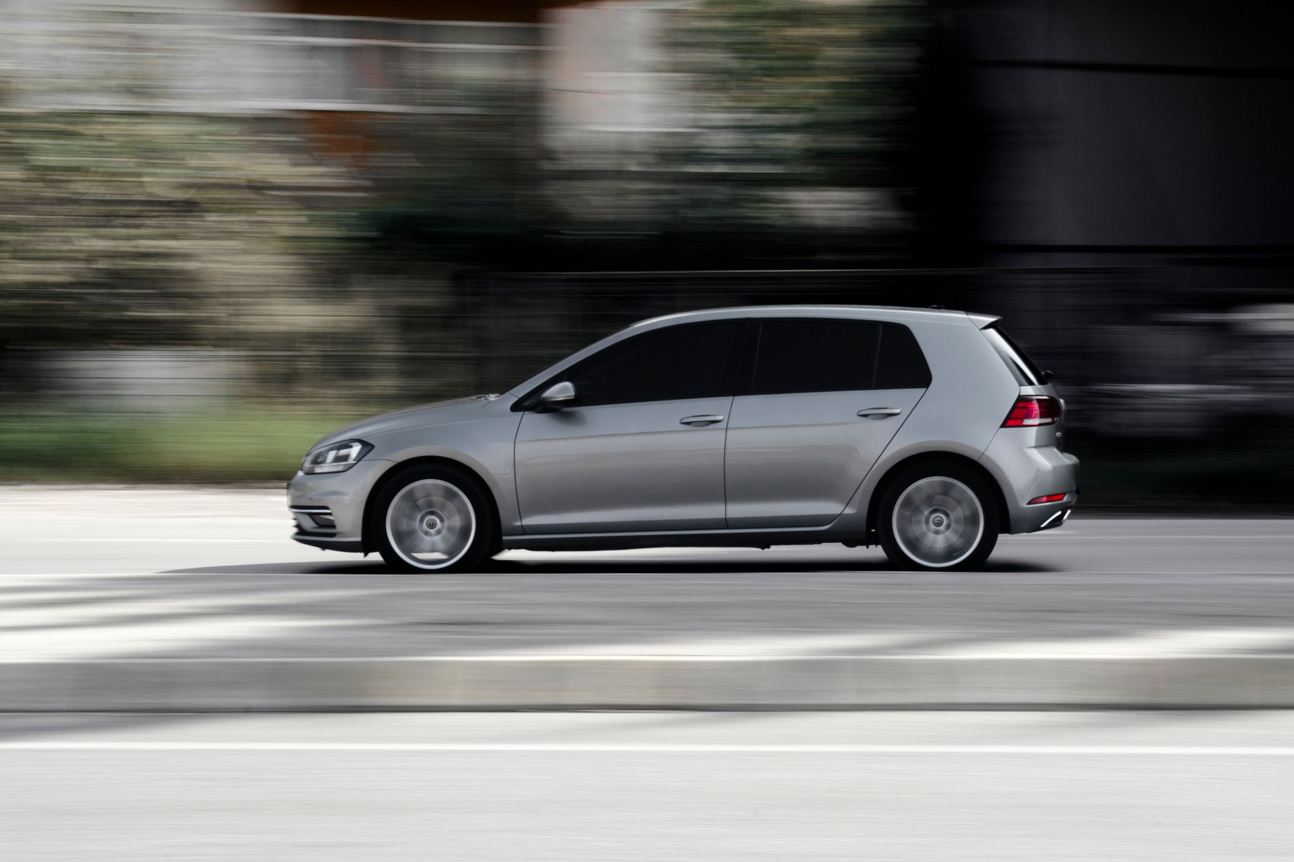 Sleek silver hatchback speeding in motion on a road, captured in a dynamic side view.