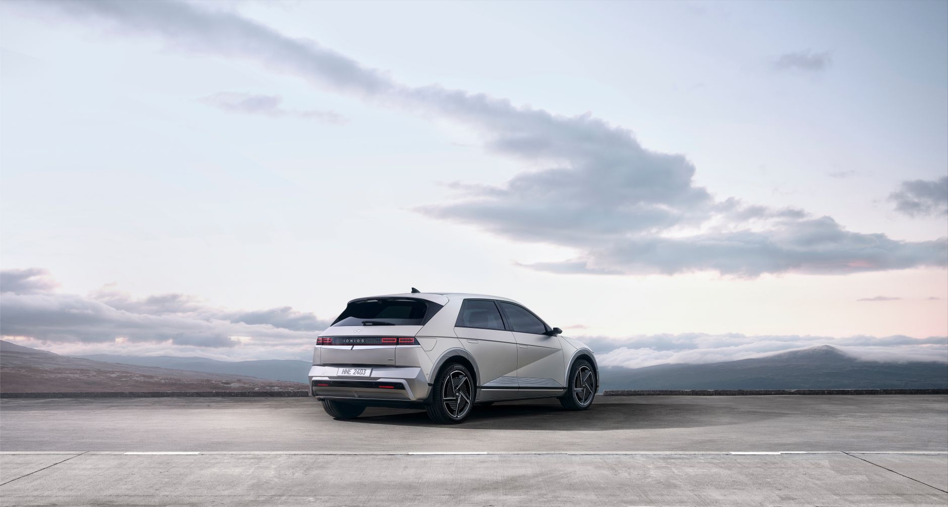 A sleek white electric SUV parked on an open road with a scenic backdrop of mountains and sky.
