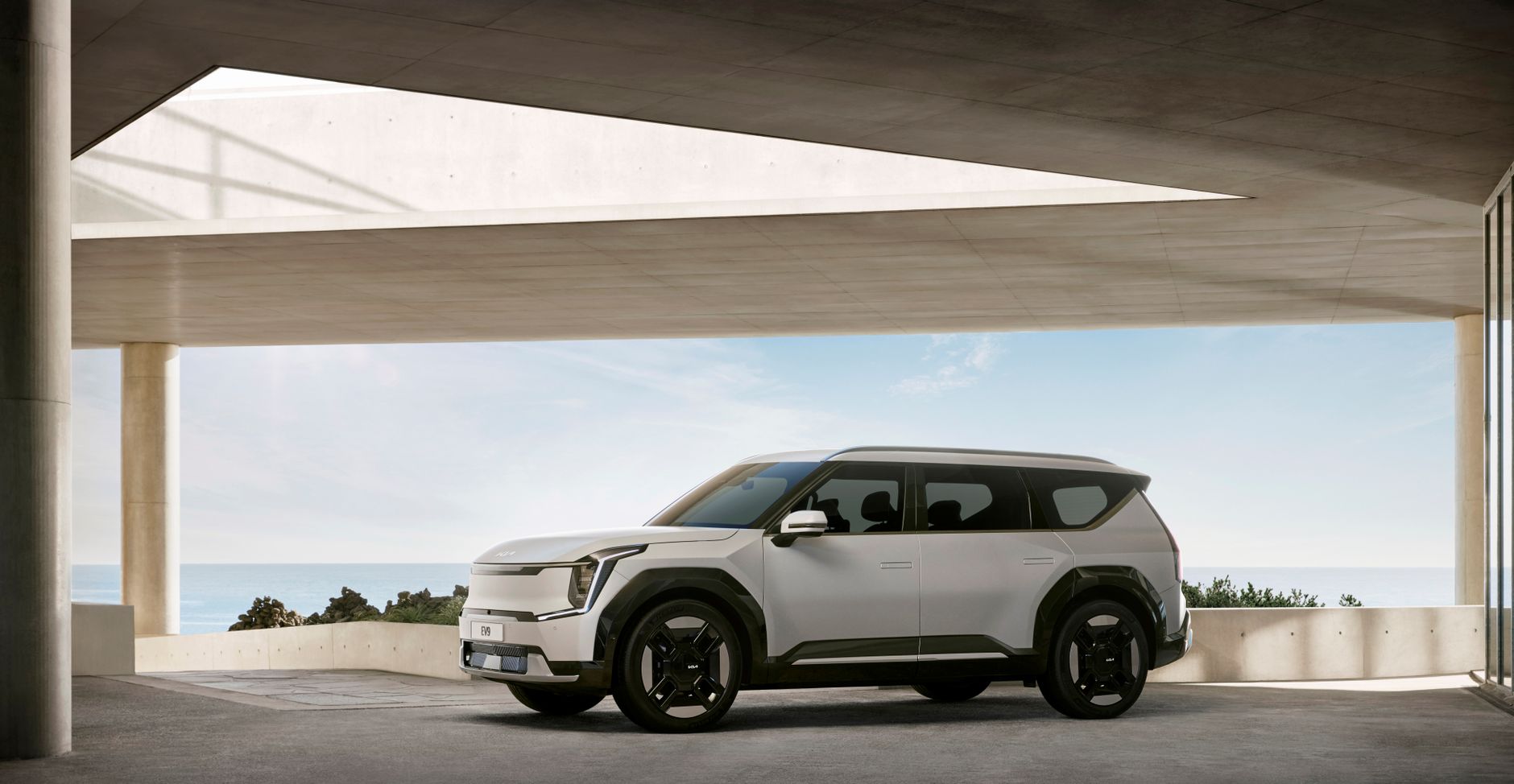 A luxurious white SUV showcased in a minimalist, concrete architectural setting with sea view.
