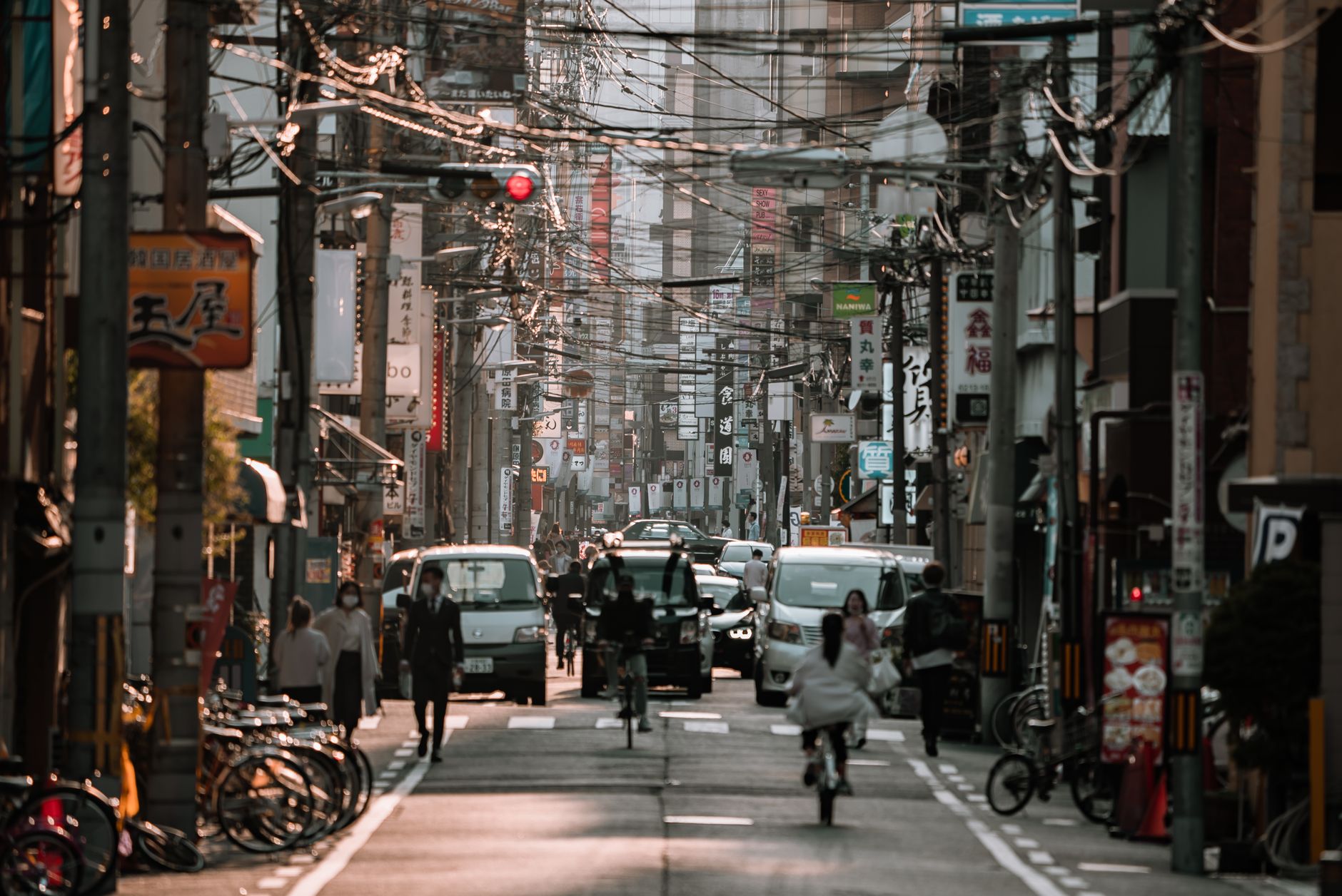 Busy street in Japan filled with cars, cyclists, and pedestrians amidst electric lines.