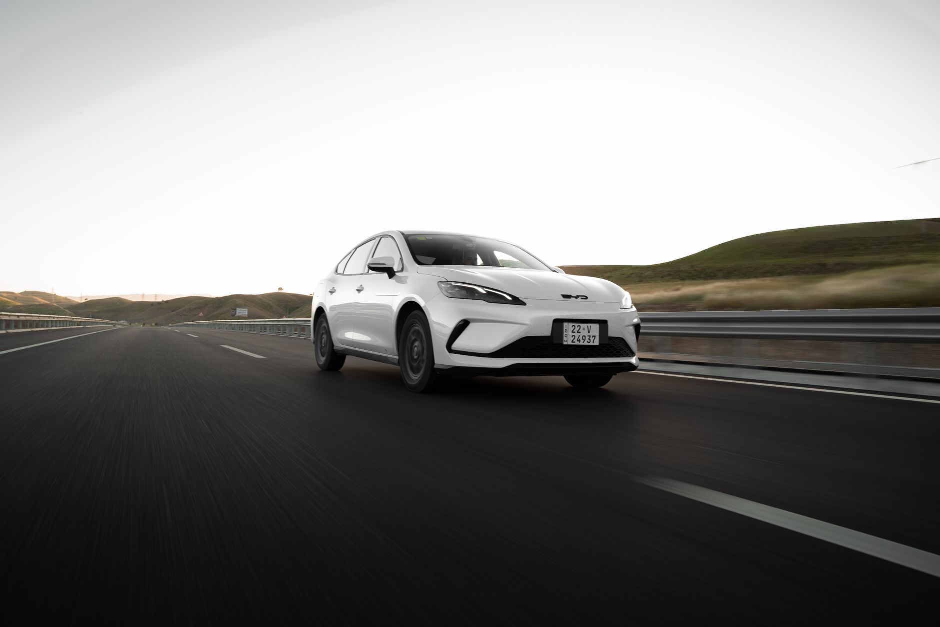 A modern white car drives on an open highway at dawn, highlighting sleek design and open road adventure.