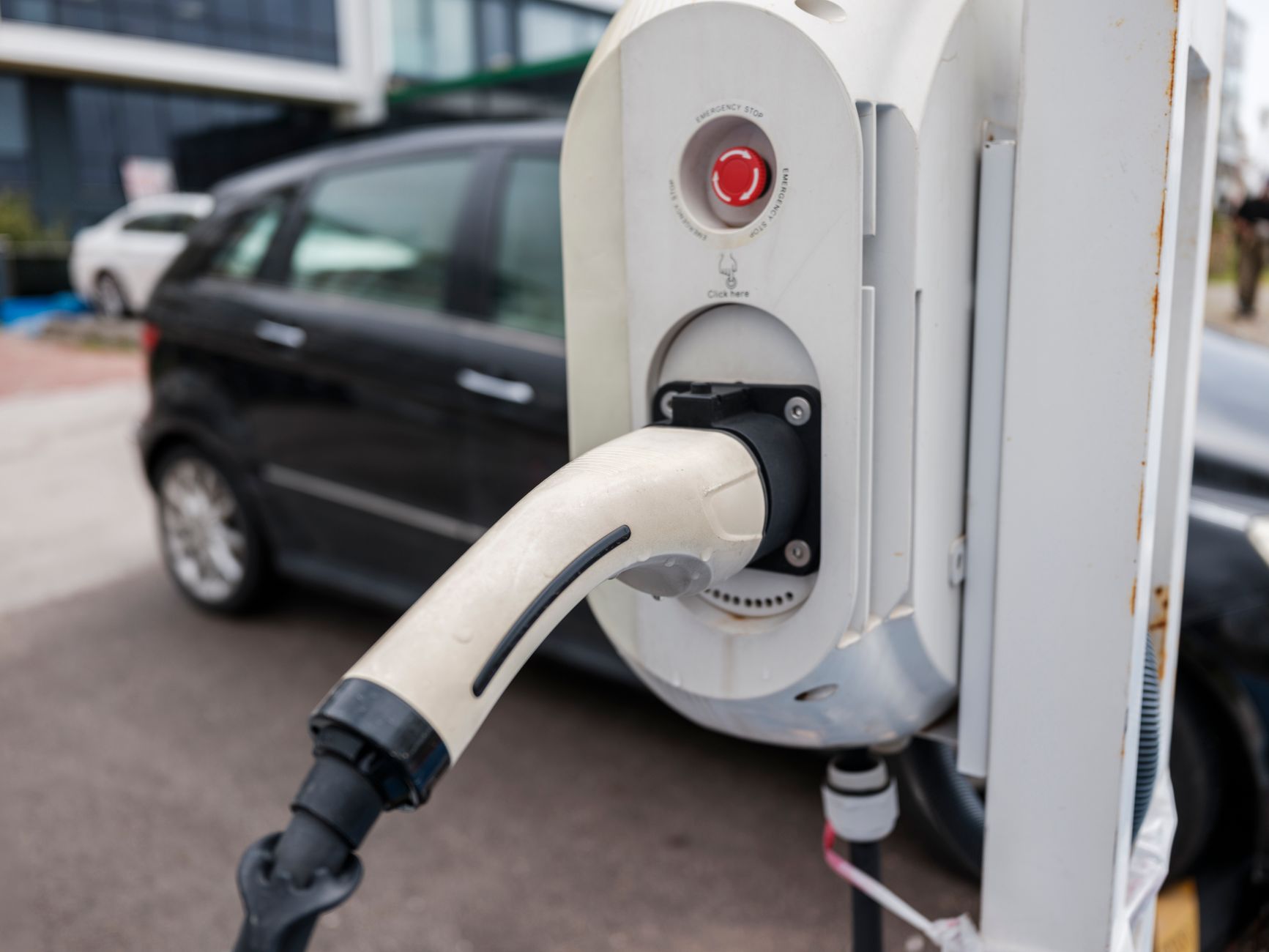 Close-up view of an electric car charging station with a plugged-in charger and cars in an urban environment.