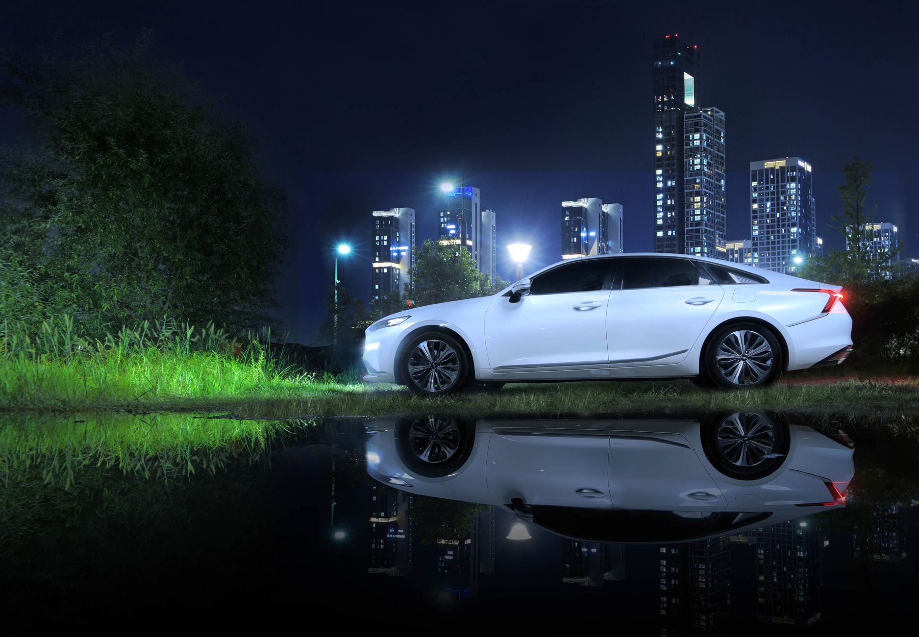 A white sedan reflecting in water with a modern city skyline illuminated at night.