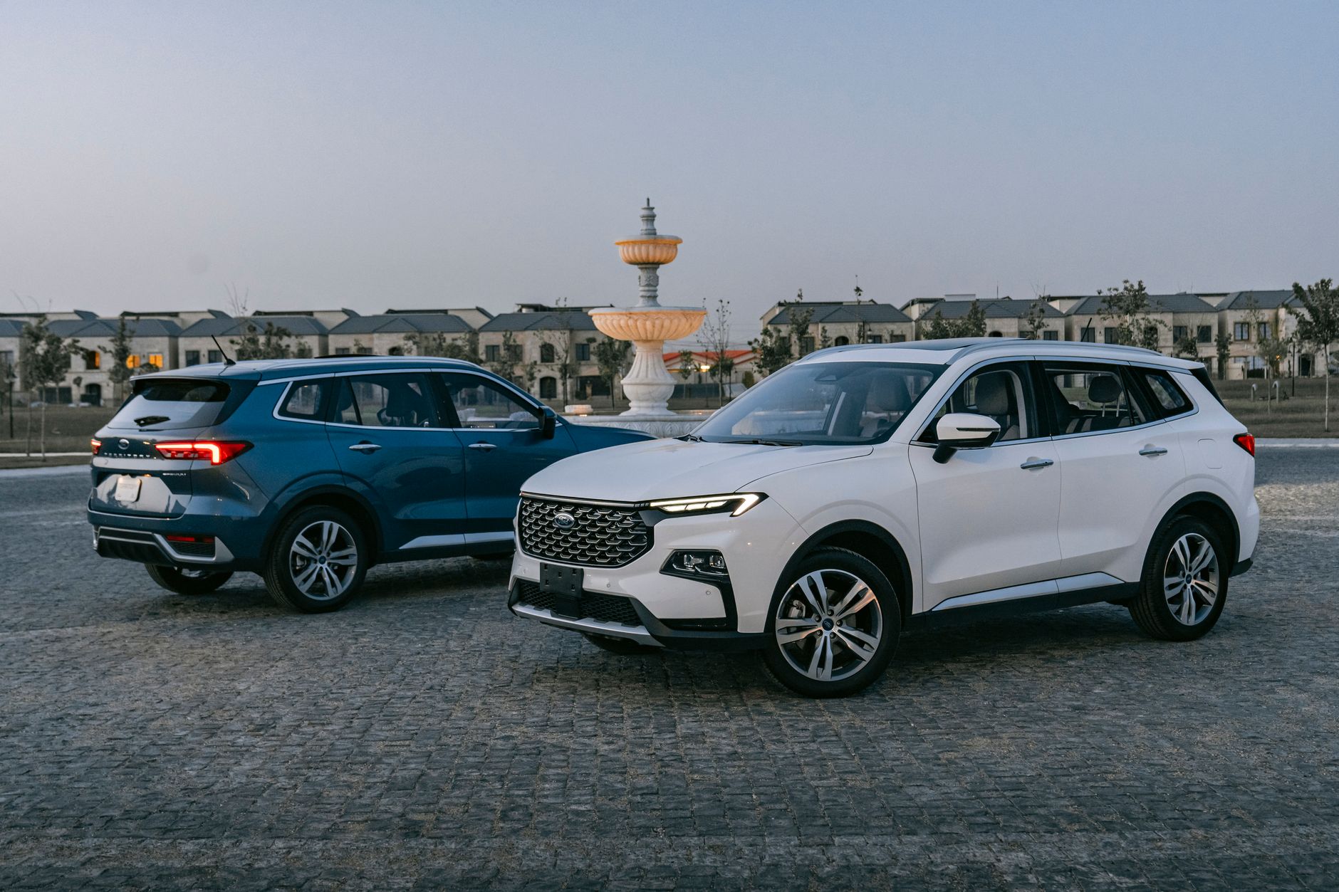 Two modern SUVs parked in a stylish plaza with a decorative fountain, showcasing contemporary automotive design.
