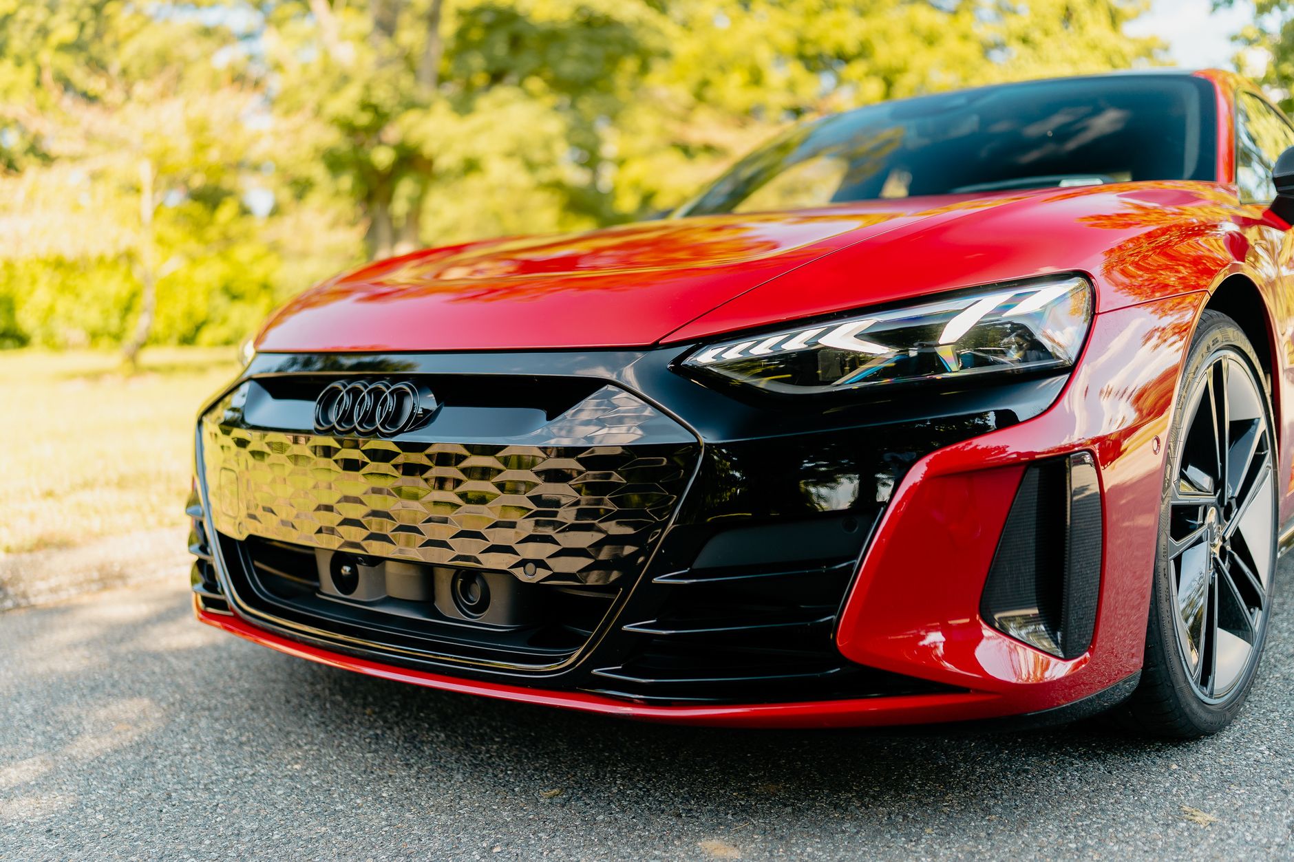 Close-up of a luxurious red electric car outdoors with sunlight reflecting on its shiny surface.