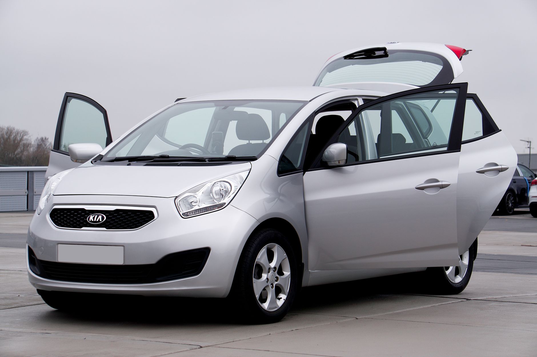 Silver Kia hatchback car photographed with doors open, parked outdoors on a cloudy day.