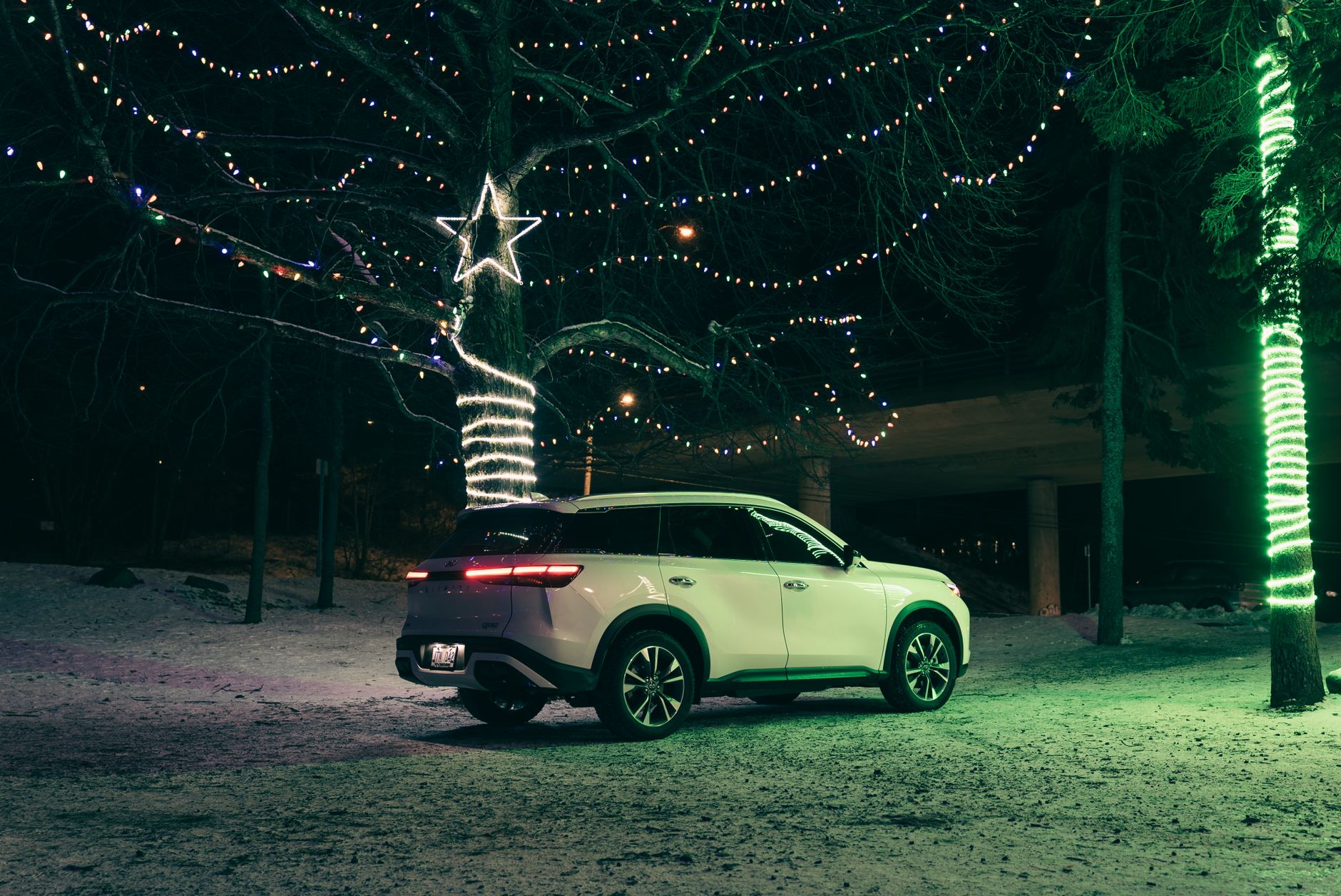 A white SUV parked in a snowy landscape adorned with festive Christmas lights at night.
