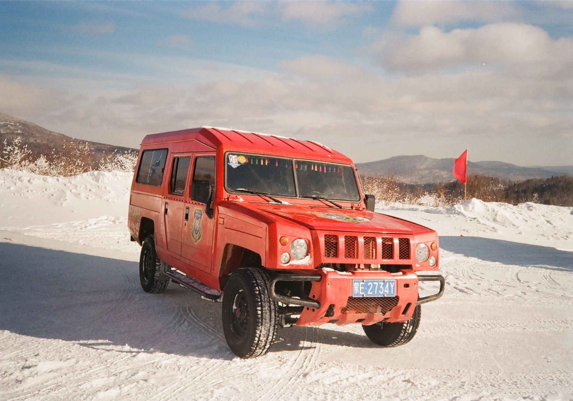 A vibrant red SUV is parked on a snowy landscape in Harbin, China, during the winter.