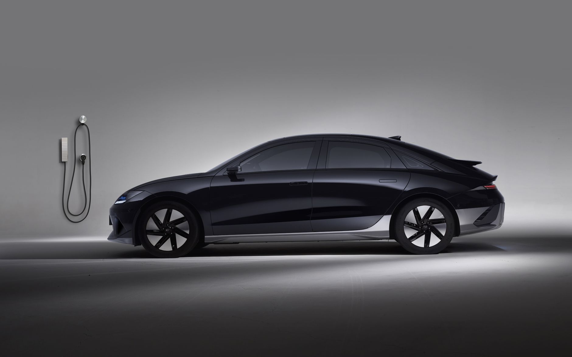 Side view of a black electric car in a studio, showcasing sleek design and charging station.