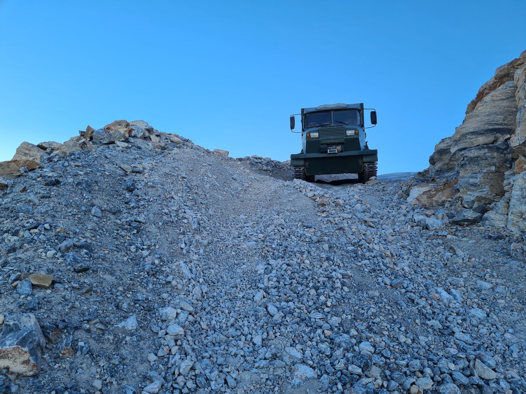 A rugged off-road truck climbs a steep, rocky hill in a barren landscape.