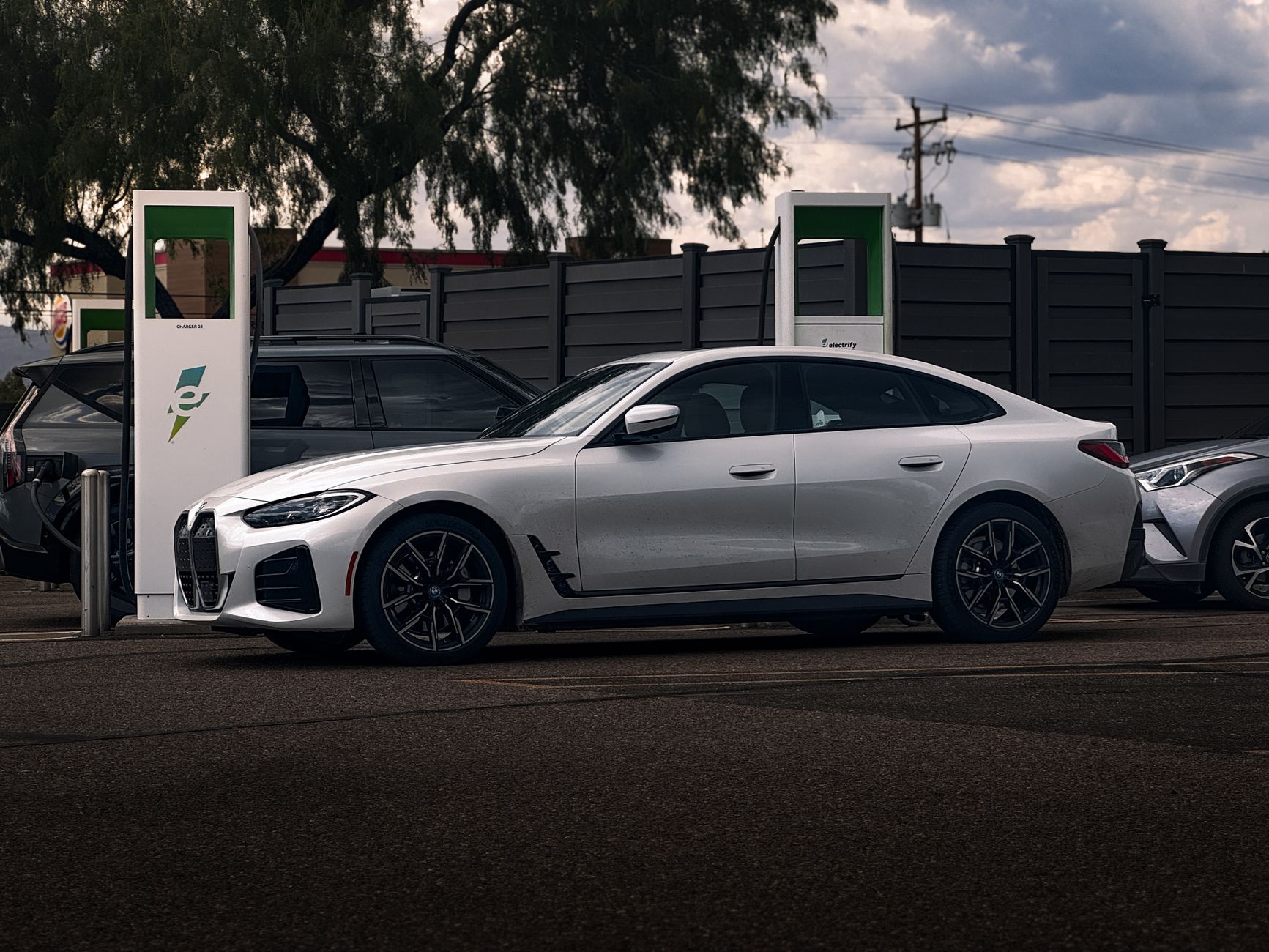 A sleek white coupe parked at an electric charging station outdoors on a cloudy day.