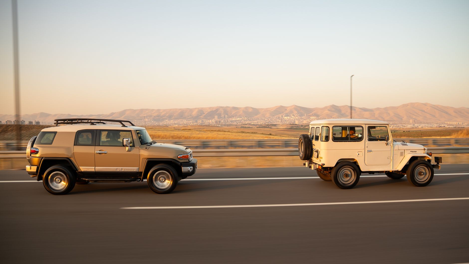 Two SUVs driving on a highway near mountains during daylight.