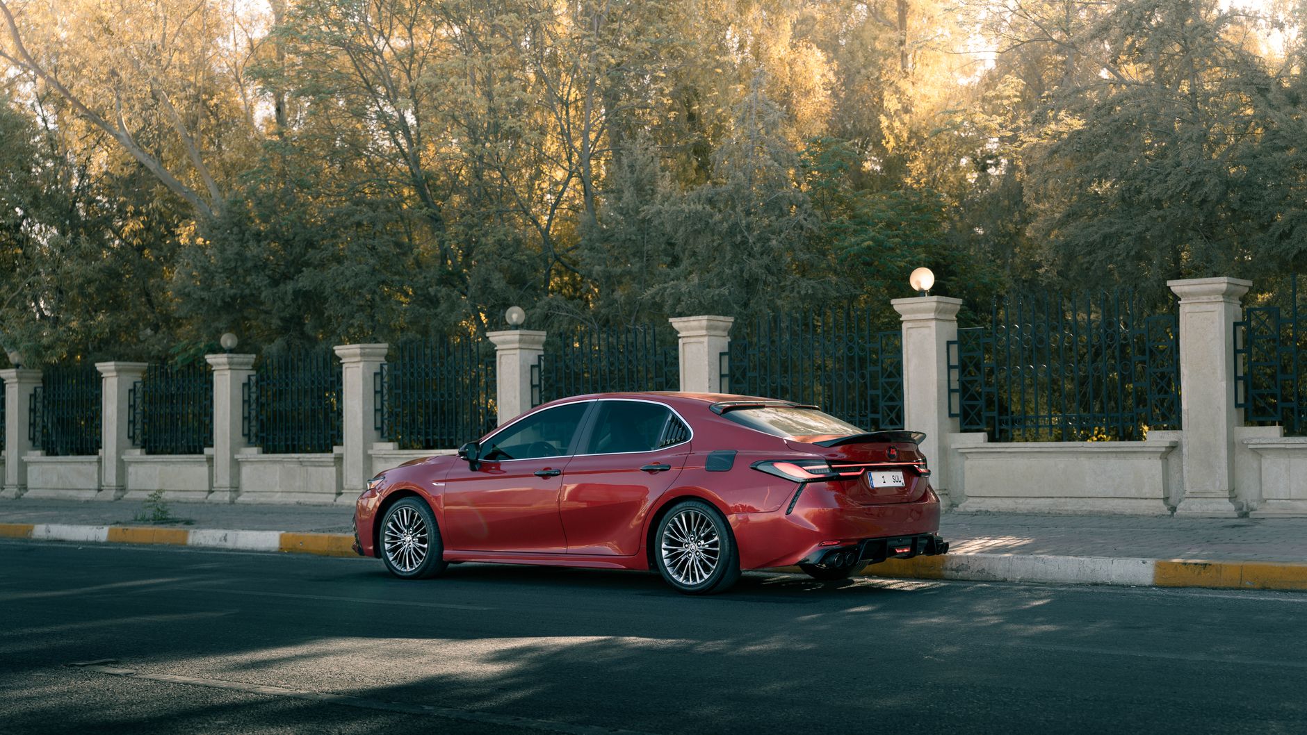 Stylish red sedan car parked beside ornate fence in sunlight, showcasing modern design.