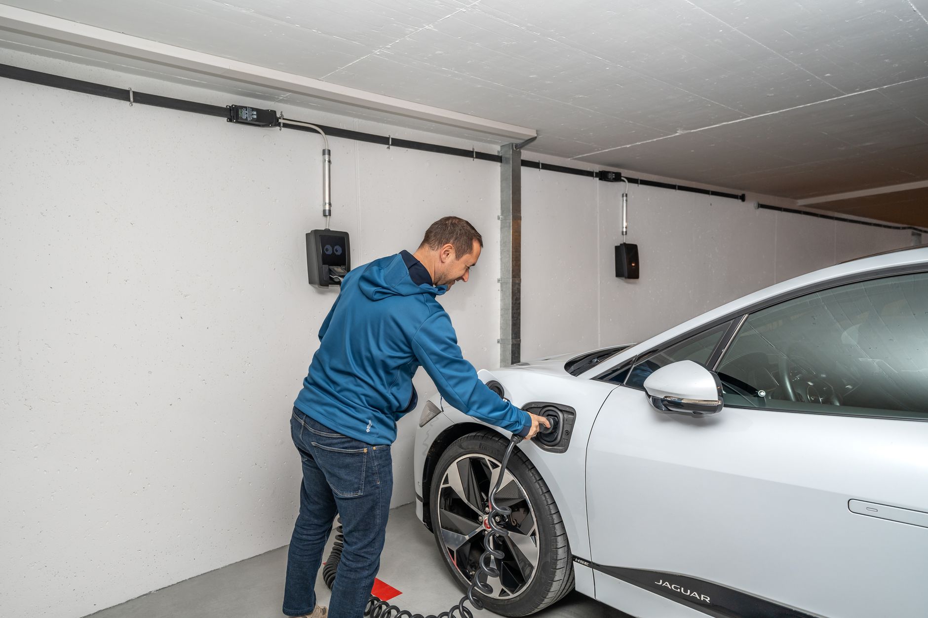 A man connects an electric car to a charging station in a modern indoor garage setting.