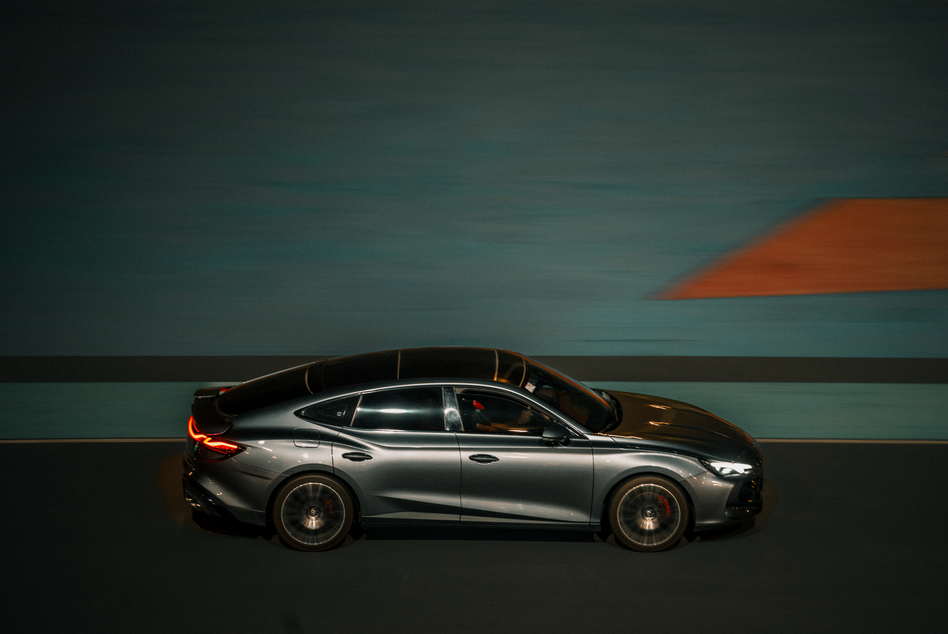 Dynamic panning shot of a sleek car driving through the streets of Kuwait City at night.