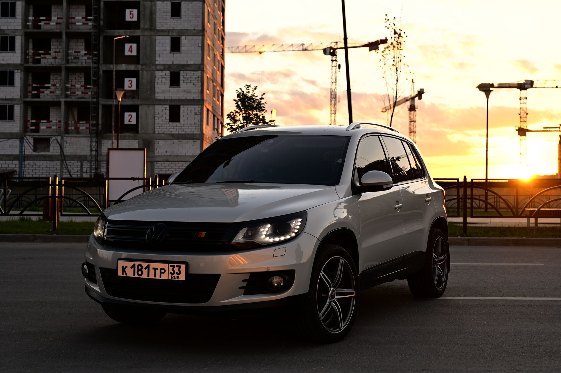 A Volkswagen SUV parked outdoors at sunset with cranes and a building under construction in the background.