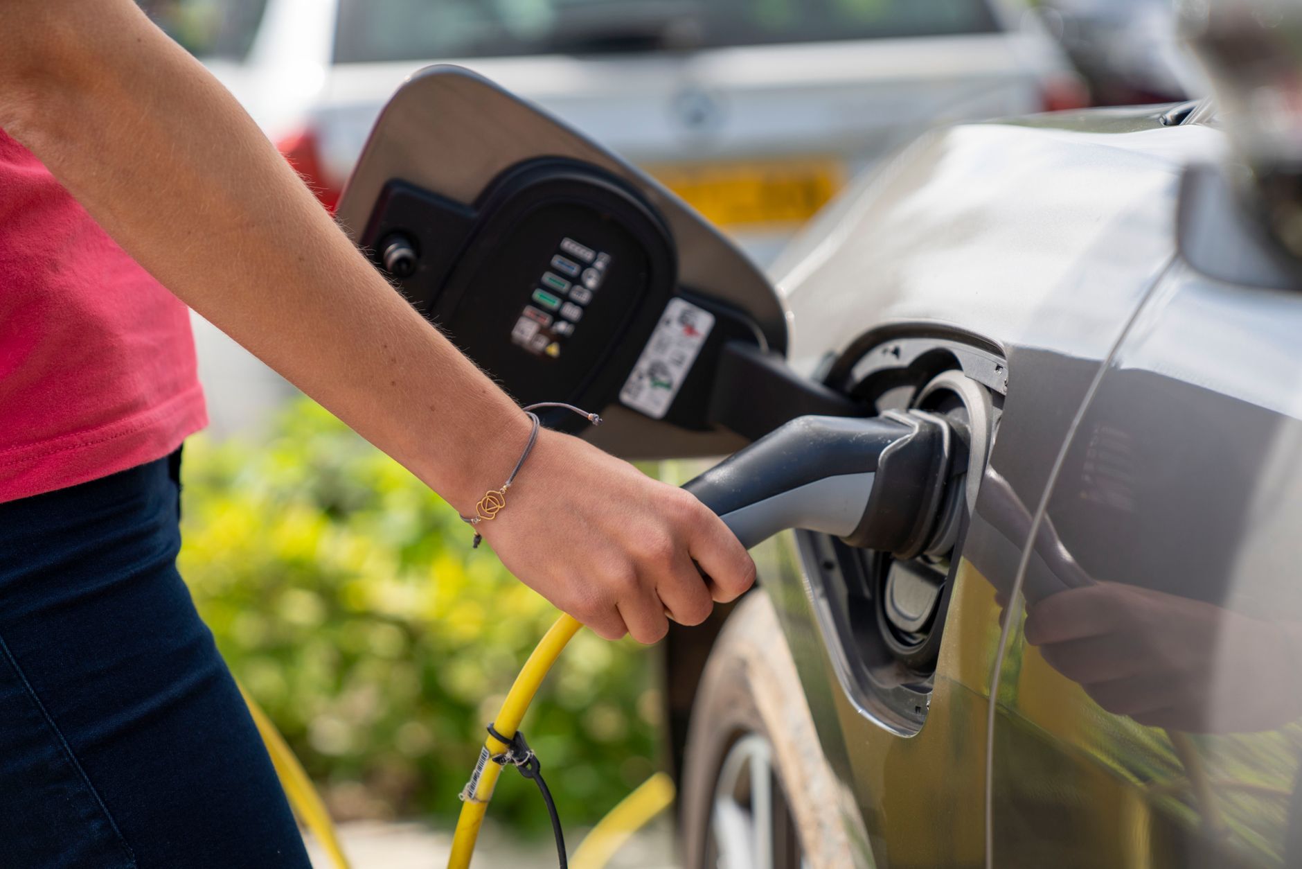 Close-up of a person plugging in an electric car at a charging station outdoors.