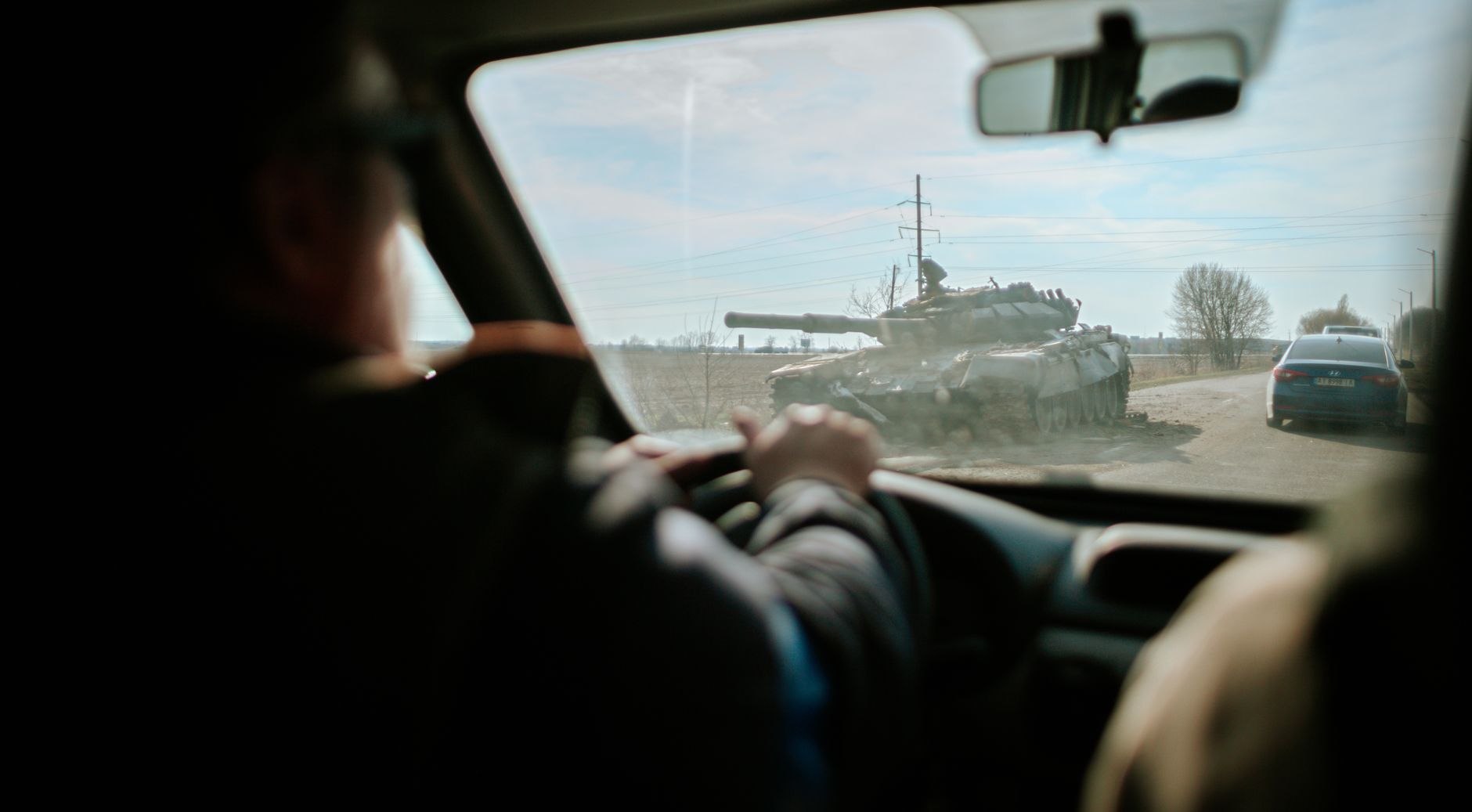 View from inside a car driving past a military tank on a road in Ukraine.
